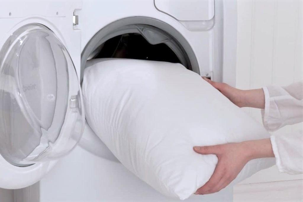 White pillow being placed into a washing machine for cleaning