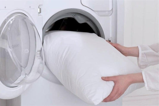 White pillow being placed into a washing machine for cleaning
