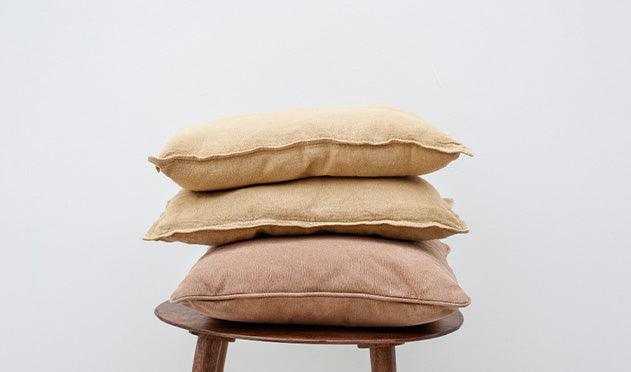 Stacked beige and brown pillows on wooden stool, luxury bedding essentials
