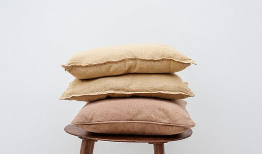 Stacked beige and brown pillows on wooden stool, luxury bedding essentials