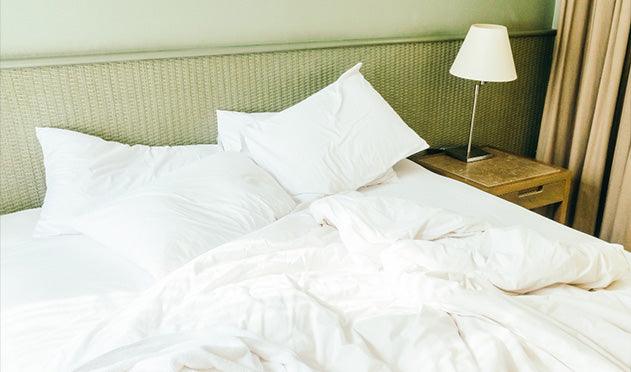 White Egyptian cotton sheets and pillows on a cozy bed with wicker headboard, styled for luxury comfort.