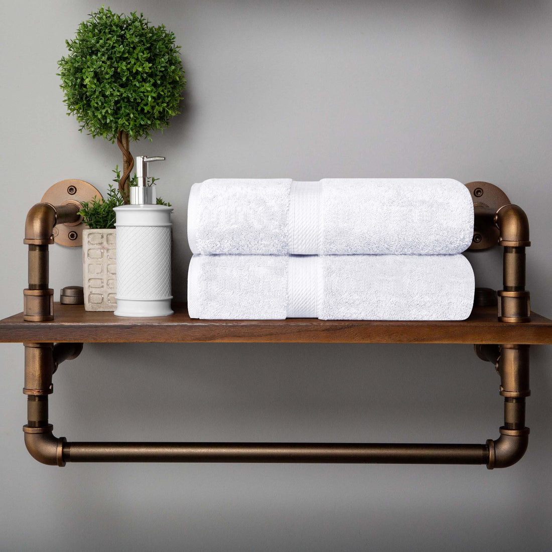 Soft white bath towels stacked on rustic shelf with greenery and soap dispenser