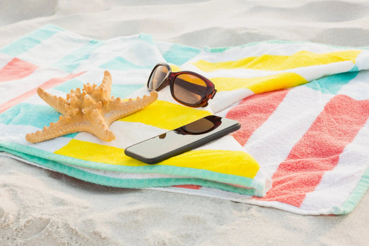 Colorful beach towel with starfish, sunglasses, and phone on sandy shore