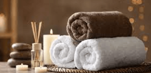 Soft Egyptian cotton bath towels in white and brown, rolled on woven tray with candles and reed diffuser